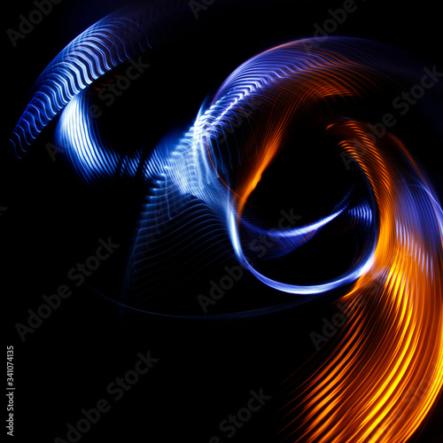 Long exposure photograph of multicolored light trails forming a complex twisted geometric pattern of parallel lines against a dark background. Only photo, no illustration.