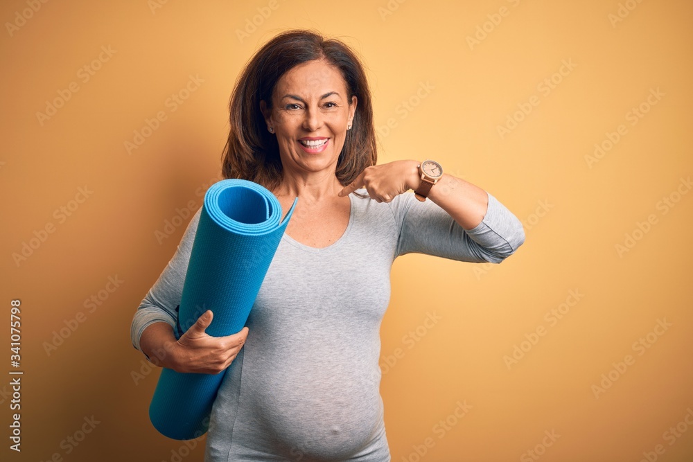 Middle age pregnant woman expecting baby holding yoga mat for healthy lifestyle with surprise face pointing finger to himself Middle age pregnant woman expecting baby holding yoga mat for healthy lifestyle with surprise face pointing finger to himself