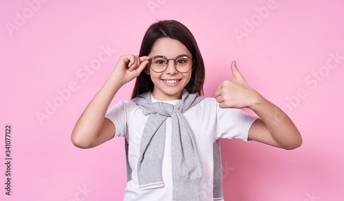 Cute fashionable emotional girl with glasses in a basic T-shirt on a pink background.