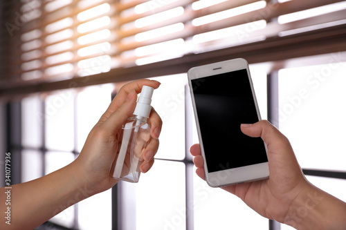 Φωτογραφία Woman sanitizing smartphone with antiseptic spray indoors, closeup