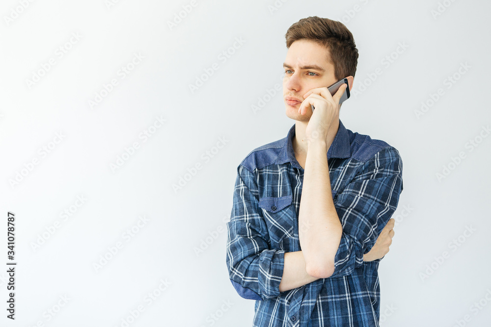 A young man talking on the phone on a light gray background. Man thought A young man talking on the phone on a light gray background. Man thought