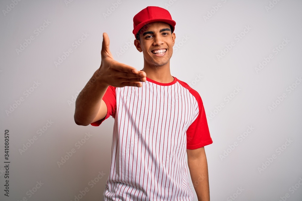Young handsome african american sportsman wearing striped baseball t-shirt and cap smiling friendly offering handshake as greeting and welcoming. Successful business.