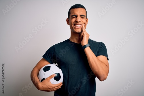 Handsome african american man playing footbal holding soccer ball over white background touching mouth with hand with painful expression because of toothache or dental illness on teeth. Dentist