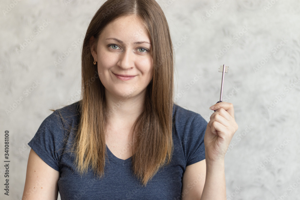 Obraz premium Beautiful young woman with long loose hair with a key in her hand. Attractive girl received a key to a new apartment, flat, home or house. Happy Lady is happy to move or approving mortgage