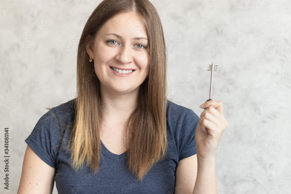 Beautiful young woman with long loose hair with a key in her hand. Attractive girl received a key to a new apartment, flat, home or house. Happy Lady is happy to move or approving mortgage Beautiful young woman with long loose hair with a key in her hand. Attractive girl received a key to a new apartment, flat, home or house. Happy Lady is happy to move or approving mortgage