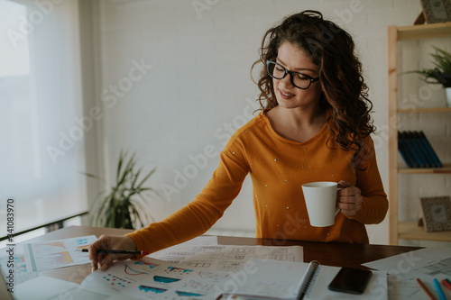 Slika na platnu Beautiful young statistician is analyzing data while having coffee at office
