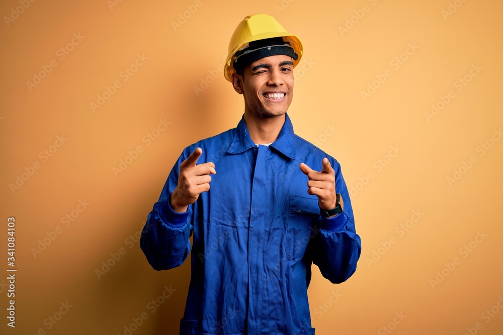 Young handsome african american worker man wearing blue uniform and security helmet pointing fingers to camera with happy and funny face. Good energy and vibes.