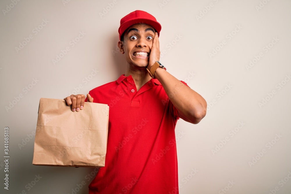 Young handsome african american delivery man holding paper bag with takeaway food stressed with hand on head, shocked with shame and surprise face, angry and frustrated. Fear and upset for mistake. Young handsome african american delivery man holding paper bag with takeaway food stressed with hand on head, shocked with shame and surprise face, angry and frustrated. Fear and upset for mistake.
