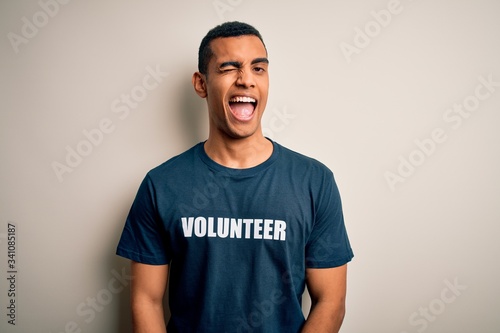Young handsome african american man volunteering wearing t-shirt with volunteer message winking looking at the camera with sexy expression, cheerful and happy face.