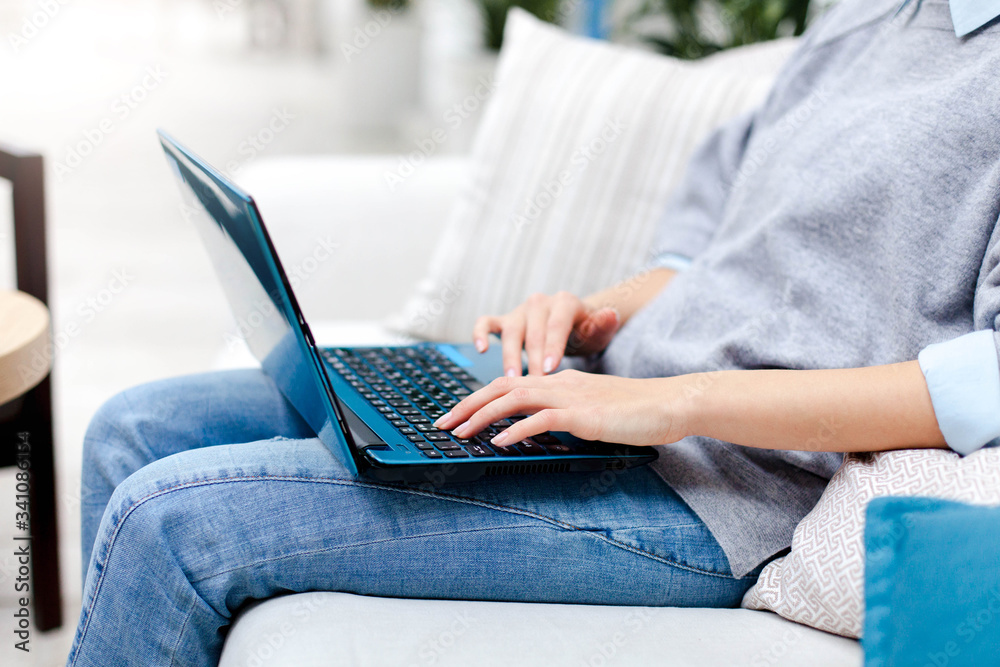 Fototapeta premium Remote working from home office. Freelancer workplace with laptop in living room. Concept of distance learning, teleworking, self isolation, female business, shopping online. Close up of woman hands.