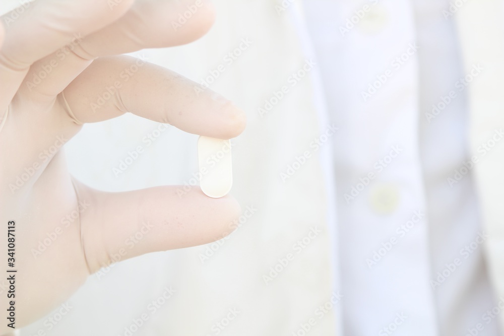 Hand in surgical glove holding a pill Hand in surgical glove holding a pill