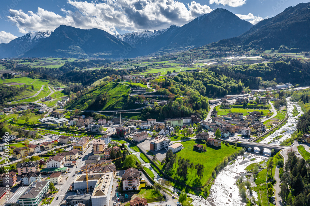 Aerial view of valley Cares, Trentino, green slopes of the mountains of Italy, huge clouds over a valley, roof tops of houses, Dolomites on background, bridges, river and roads, spring colors