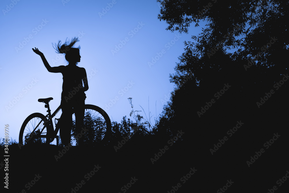 Obraz premium silhouette of a young girl with a bicycle at sunset in the middle of nature