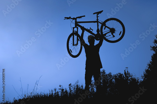 Silhouette of a man lifting a bicycle above himself