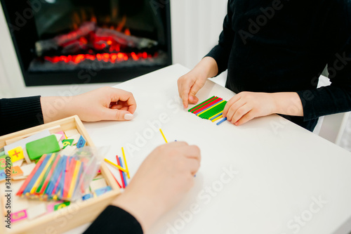 mom plays with her daughter at the table with multi-colored wooden chopsticks, getting ready for school playing, learning the score