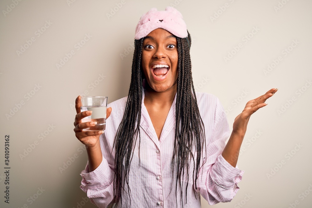 Young african american woman wearing pajama and eye mask drinking glass of water at night very happy and excited, winner expression celebrating victory screaming with big smile and raised hands Young african american woman wearing pajama and eye mask drinking glass of water at night very happy and excited, winner expression celebrating victory screaming with big smile and raised hands