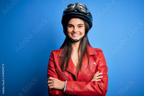 Young beautiful brunette motorcycliste woman wearing motorcycle helmet and jacket happy face smiling with crossed arms looking at the camera. Positive person. © Krakenimages.com