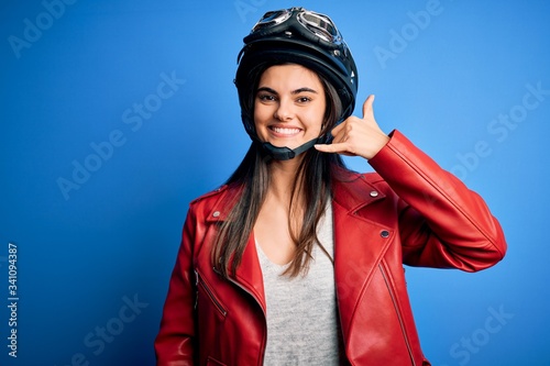 Young beautiful brunette motorcycliste woman wearing motorcycle helmet and jacket smiling doing phone gesture with hand and fingers like talking on the telephone. Communicating concepts. © Krakenimages.com