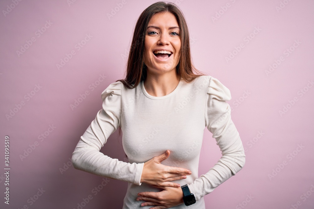 Young beautiful woman with blue eyes wearing casual white t-shirt over pink background smiling and laughing hard out loud because funny crazy joke with hands on body. Young beautiful woman with blue eyes wearing casual white t-shirt over pink background smiling and laughing hard out loud because funny crazy joke with hands on body.