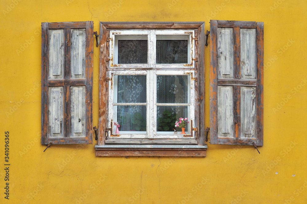 Window frame with shutters in yellow facade.