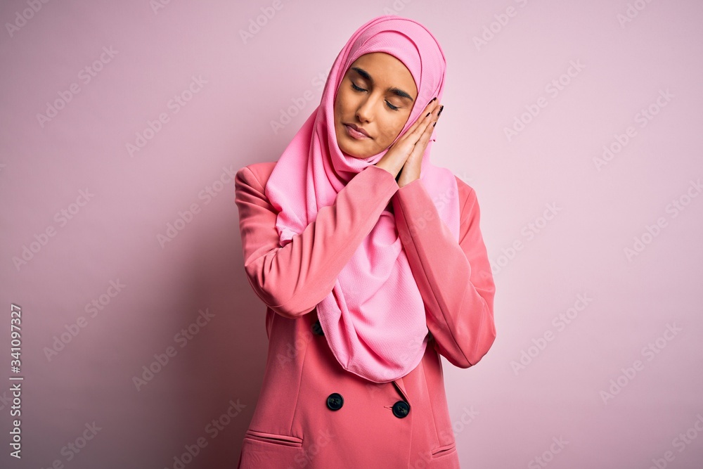 Young beautiful brunette businesswoman wearing pink muslim hijab and business jacket sleeping tired dreaming and posing with hands together while smiling with closed eyes. Young beautiful brunette businesswoman wearing pink muslim hijab and business jacket sleeping tired dreaming and posing with hands together while smiling with closed eyes.