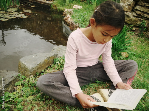 Métis little sitting reading on the grass by the pond photo