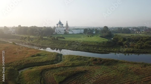 4K aerial dense sunny summer morning video of Suzdal churches, buildings, hills, fields and cathedrals located on Kamenka River shore in Vladimir Region, Russia