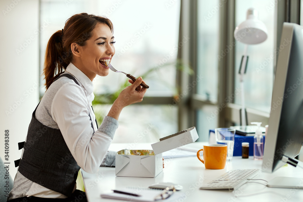 Happy businesswoman eating on a lunch break in the office.