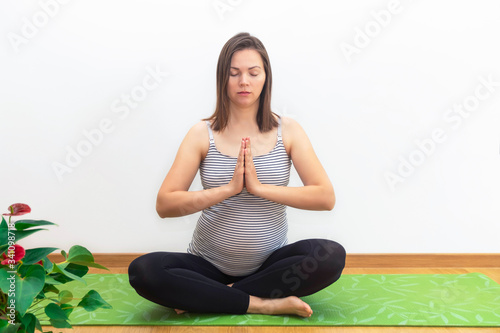 Pregnancy yoga concept. Young pregnant woman exersizing yoga in lotus pose at home