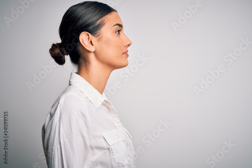Fotografie Young beautiful brunette woman wearing casual shirt over isolated white background looking to side, relax profile pose with natural face with confident smile