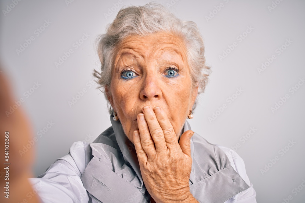 Senior beautiful grey-haired woman making selfie by camera over isolated white background cover mouth with hand shocked with shame for mistake, expression of fear, scared in silence, secret concept Senior beautiful grey-haired woman making selfie by camera over isolated white background cover mouth with hand shocked with shame for mistake, expression of fear, scared in silence, secret concept