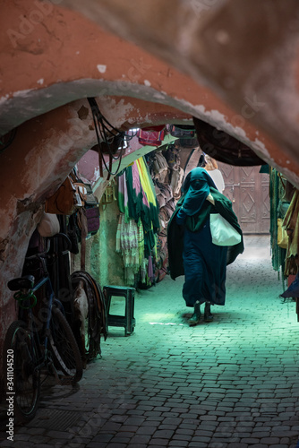 Muslim woman walking down passageway with shops, dressed in black and covering her face