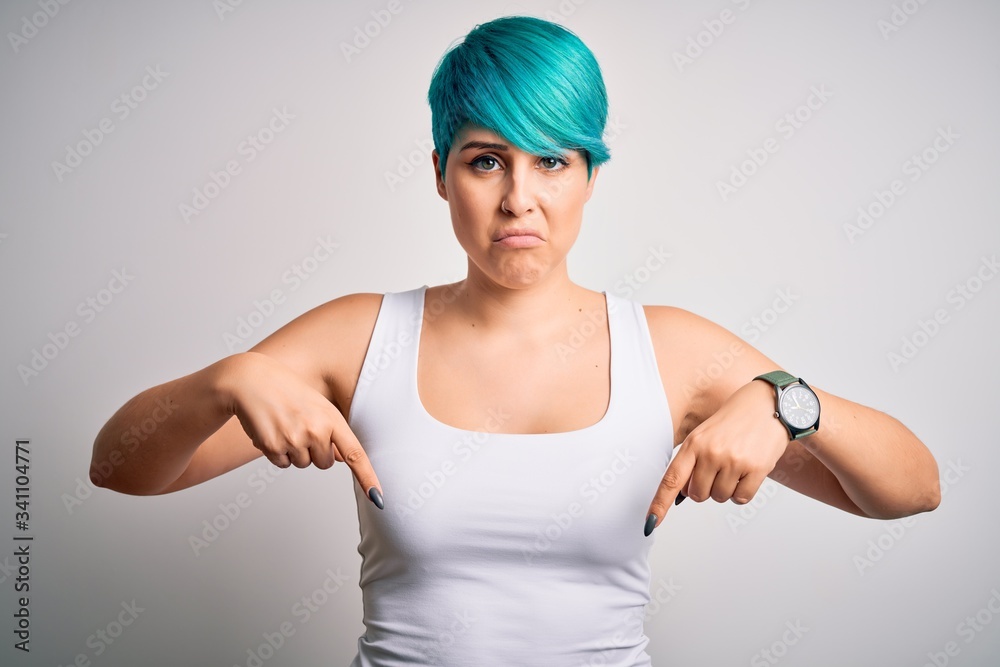 Young beautiful woman with blue fashion hair wearing casual t-shirt over white background Pointing down looking sad and upset, indicating direction with fingers, unhappy and depressed. Young beautiful woman with blue fashion hair wearing casual t-shirt over white background Pointing down looking sad and upset, indicating direction with fingers, unhappy and depressed.