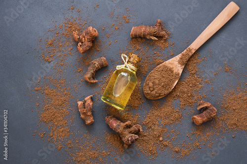 Foto Glass bottle of Galangal essential oil, root and galanga powder in wooden spoon on rustic table