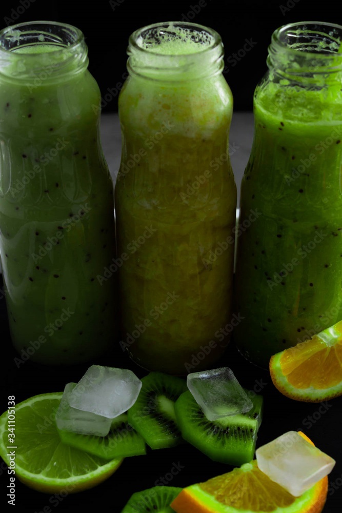 Freshly squeezed smoothie from different berries on a dark background. Green, yellow. Place for advertising. On the table are orange, kiwi, ice. Freshly squeezed smoothie from different berries on a dark background. Green, yellow. Place for advertising. On the table are orange, kiwi, ice.