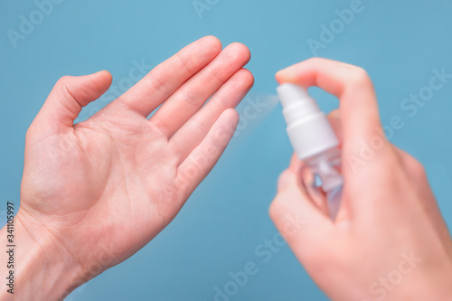 Hands spray disinfectant to clean and protect hands against viruses on blue background. Closeup of hands disinfecting smartphone. Cleaning hands with sanitizer. Pandemic background