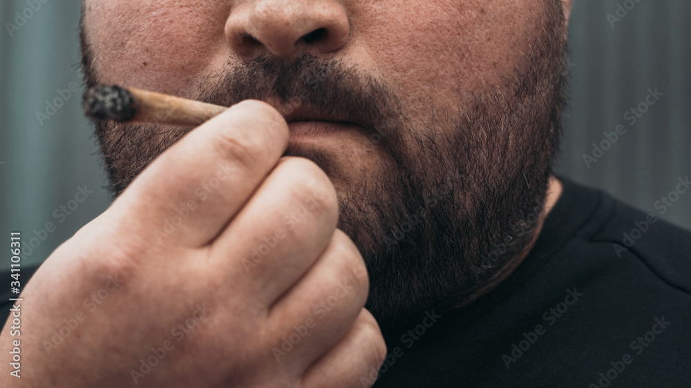 Obraz premium Man smoking real rolled marijuana or cannabis or weed joint tobacco cigarette, close up.