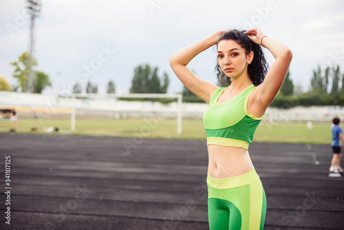 Beautiful curly girl flexing muscles in the stadium. The girl goes in for sports. Light green tracksuit © maxfotoadobe