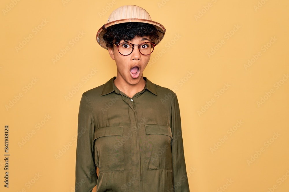 Young beautiful african american tourist woman wearing glasses and explorer hat afraid and shocked with surprise expression, fear and excited face. Young beautiful african american tourist woman wearing glasses and explorer hat afraid and shocked with surprise expression, fear and excited face.