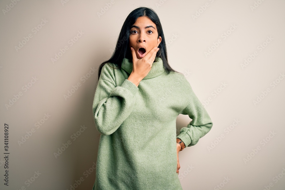 Young beautiful hispanic woman wearing green winter sweater over isolated background Looking fascinated with disbelief, surprise and amazed expression with hands on chin