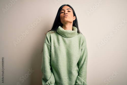 Young beautiful hispanic woman wearing green winter sweater over isolated background looking at the camera blowing a kiss on air being lovely and sexy. Love expression. © Krakenimages.com