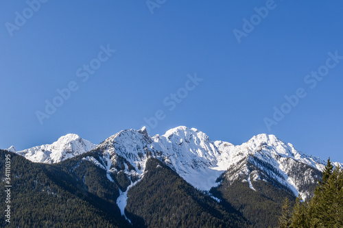 close-up view of the mountain peak with trees and snow on it sunny spring day.