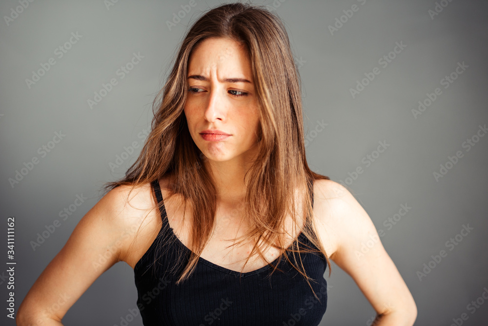 The girl with her hair in a black top looks thoughtfully to the side. To be upset, thoughtful, serious. On a gray background. Without makeup, without retouching.