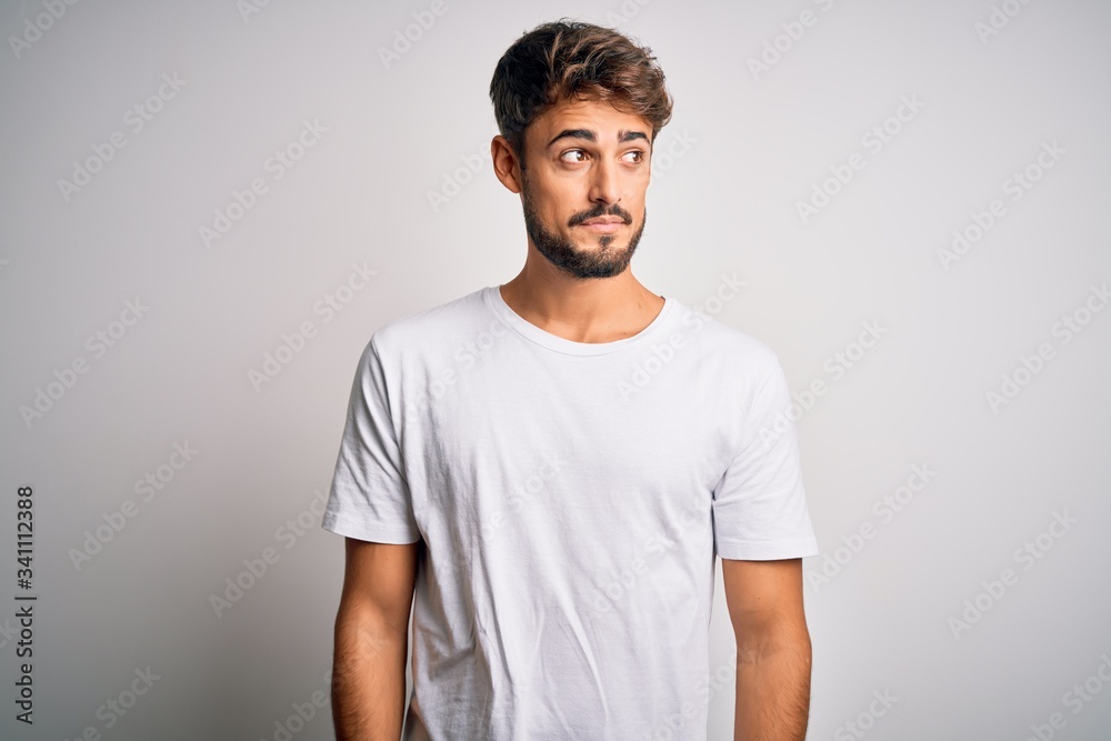 Young handsome man with beard wearing casual t-shirt standing over white background smiling looking to the side and staring away thinking. Young handsome man with beard wearing casual t-shirt standing over white background smiling looking to the side and staring away thinking.