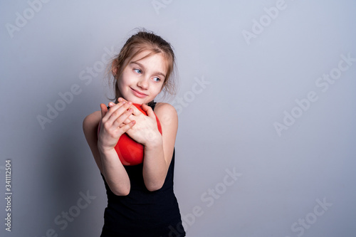 A white-skinned girl in a black training shirt holds a red gymnastic ball and presses it to her chest. Love for sports. Place for text.