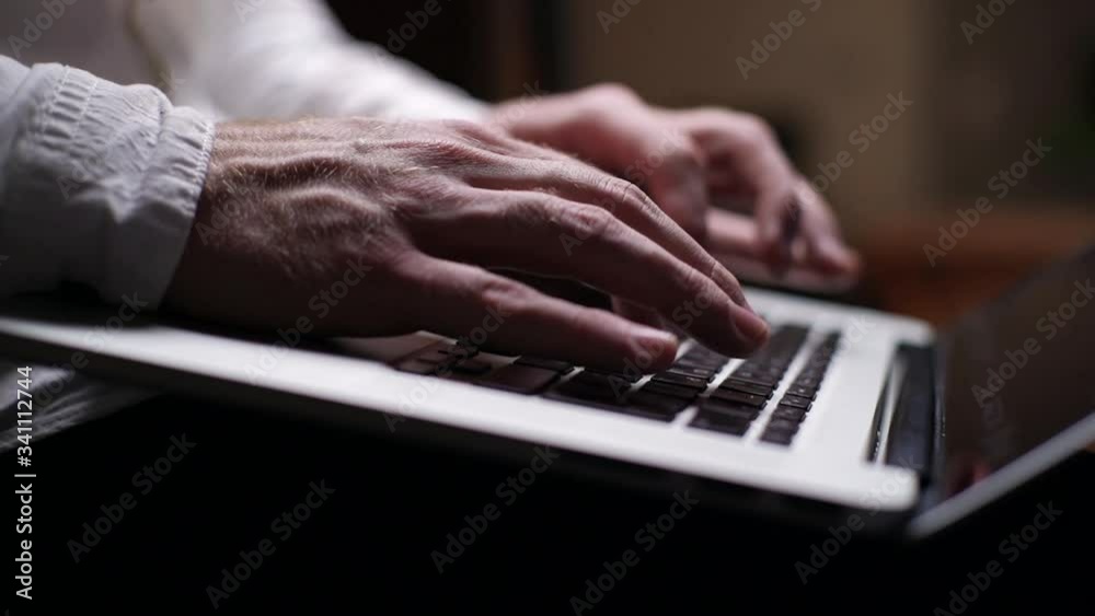 Man typing on keyboard of computer in dark living room, close-up, no face man. Side view. Male sitting and using notebook at home. Tracking shot in slow motion. Man typing on keyboard of computer in dark living room, close-up, no face man. Side view. Male sitting and using notebook at home. Tracking shot in slow motion.
