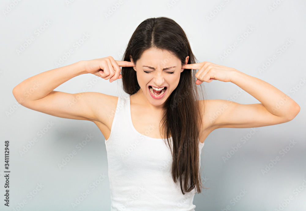 Anger young casual woman strong screaming with wild open mouth and covering the ears the fingers on blue background. Closeup Anger young casual woman strong screaming with wild open mouth and covering the ears the fingers on blue background. Closeup