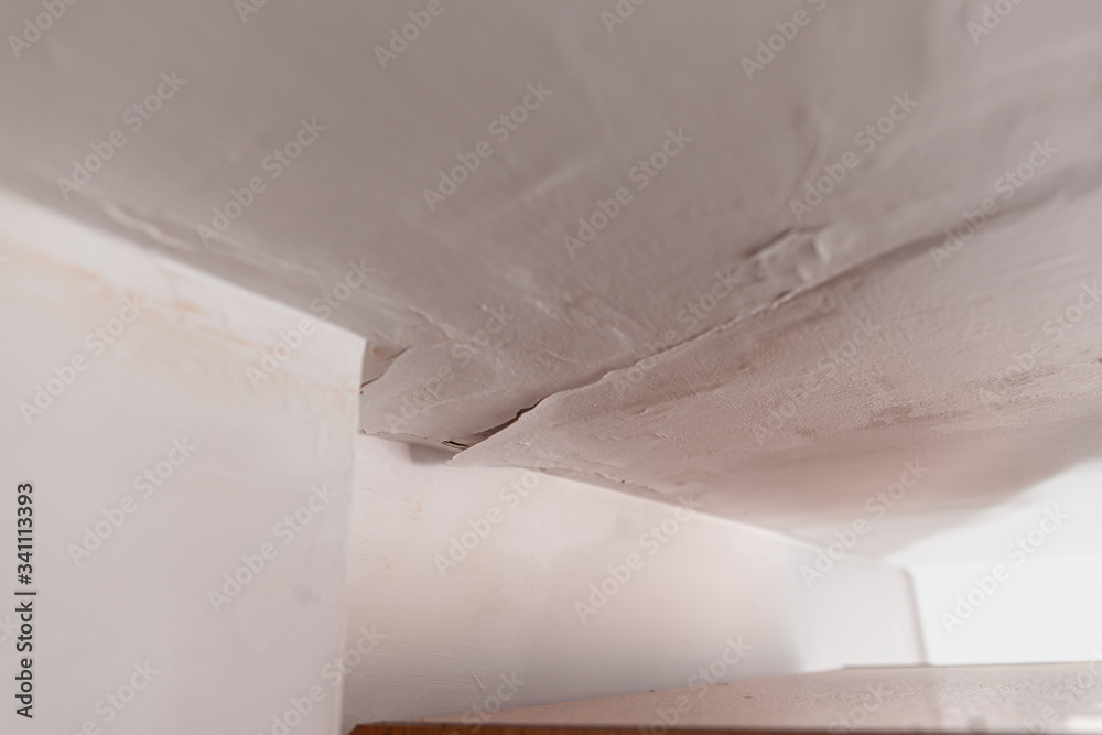 Selective focus on peeling paint on ceiling a result of roof leaking. Water damaged ceiling caused by a leaking pipe a result of substandard plumbing. A common house insurance claim