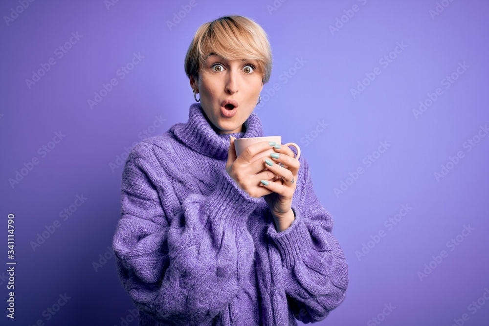Young blonde woman with short hair wearing winter sweater drinking a cup of hot coffee scared in shock with a surprise face, afraid and excited with fear expression Young blonde woman with short hair wearing winter sweater drinking a cup of hot coffee scared in shock with a surprise face, afraid and excited with fear expression
