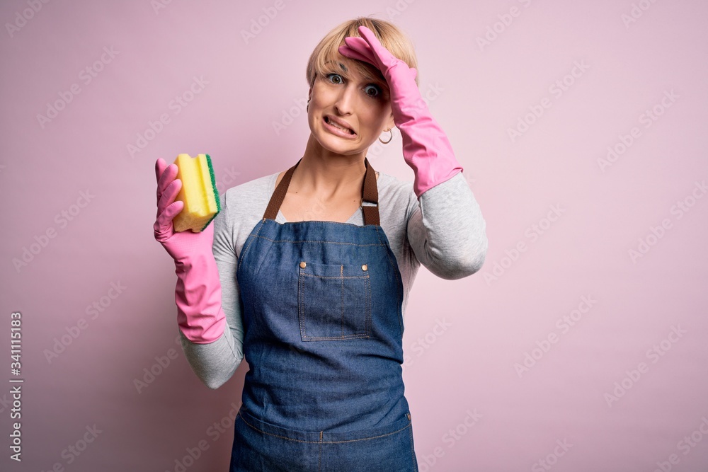 Young blonde cleaner woman with short hair wearing apron and gloves holding scrub scourer stressed with hand on head, shocked with shame and surprise face, angry and frustrated. Fear and upset Young blonde cleaner woman with short hair wearing apron and gloves holding scrub scourer stressed with hand on head, shocked with shame and surprise face, angry and frustrated. Fear and upset